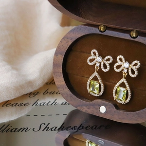 Detail of gold bow earrings with yellow teardrop crystals on a walnut jewelry box