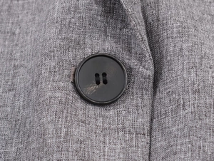 Macro shot of gray herringbone fabric texture and black button detail on the blazer jacket