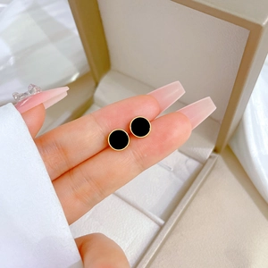 Macro detail of minimalist black round stud earrings with elegant gold trim held by hand