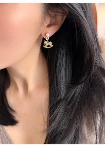 Detail of rocking horse earring with gold plating, pearl, and pavé set crystals on model