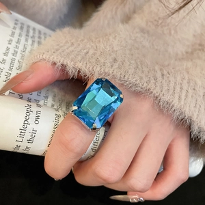 Macro shot of silver ring with step-cut rectangular blue gemstone and prong setting
