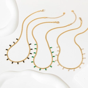 Gold snake chain necklaces with emerald and crystal pendants on a white display stand