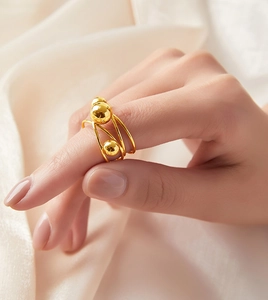 Detail of gold-plated multi-layer ring featuring golden beads on a soft fabric background