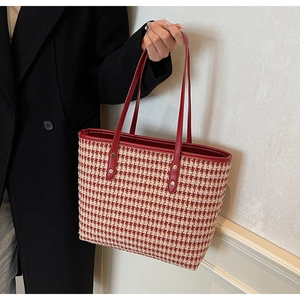 Close-up of a red and white houndstooth tote bag with leather handles on a black coat