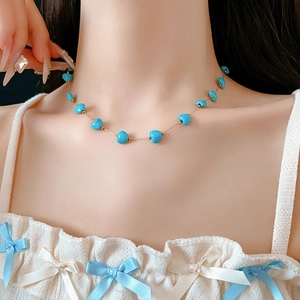 Close-up of a heart-shaped turquoise bead necklace on a model wearing white lace