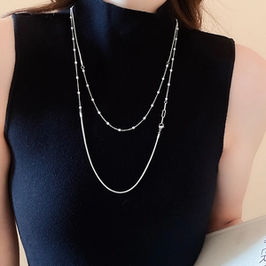 Close-up of layered silver snake chain and bead necklace on black turtleneck sweater