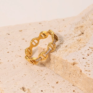 Gold chain ring with micro-paved zircons and anchor link design on beige travertine