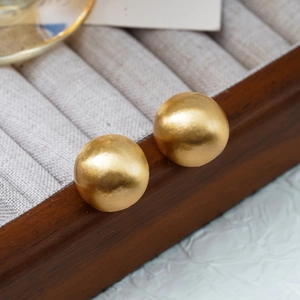 Macro shot of gold spherical stud earrings with matte texture on wooden box edge