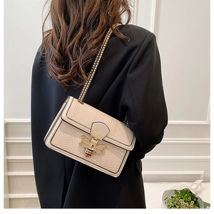 Detail of beige crocodile pattern handbag featuring a vintage gold bee clasp and metal chain