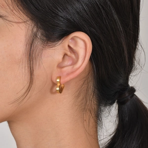 Close-up of a model wearing minimalist gold heart-shaped hoop earrings in stainless steel