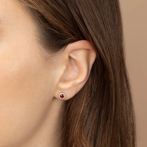 Elegant gold round stud earrings with a vibrant ruby center and diamond halo on model