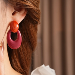 Close-up of model wearing oval hollow resin earrings in deep red and orange shades
