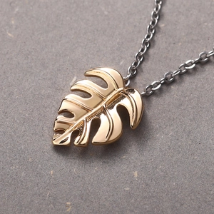 Minimalist gold monstera leaf pendant necklace with silver chain on grey background