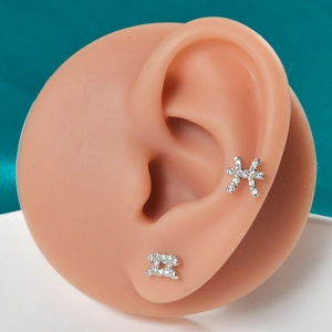 Detailed close-up of zodiac silver studs with white zircon inlay on silicone ear model