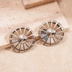 Macro view of silver geometric sunflower stud earrings on a beige travertine stone surface