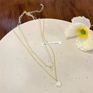 Double-layered gold necklace featuring pearls and a heart-shaped cat-eye stone pendant