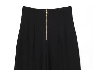 Détail de pantalon taille haute montrant la fermeture éclair en métal doré sur tissu noir