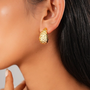 Detail of gold teardrop earring with hammered texture on female model ear
