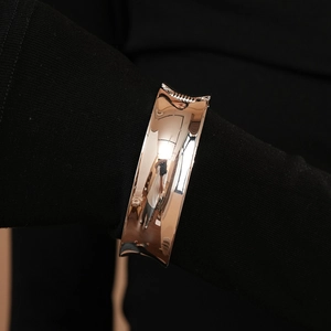 Detail of a minimalist rose gold geometric open cuff bracelet worn on a black sleeve