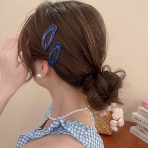 Detail of blue acetate oval hair clips with gold lettering on a female model