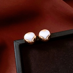 Close-up of elegant gold round stud earrings with white heart inlay on a dark background