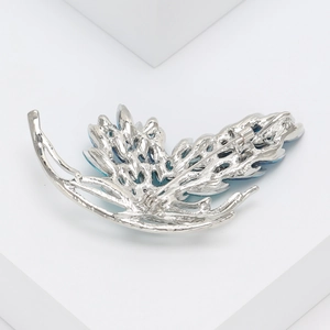 Macro detail of leaf-shaped silver brooch back with secure pin on a white platform