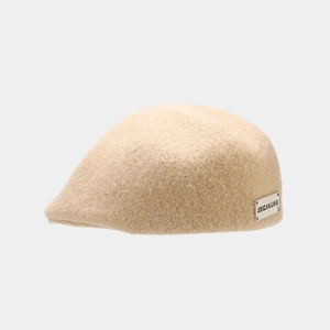 Detail of beige knitted newsboy cap featuring a silver metallic brand logo plate