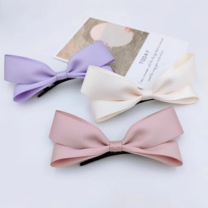 Detailed view of three satin bow hair clips in purple, beige and pink on a white surface