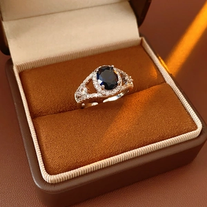 Detail of an oval blue zircon ring with halo crystals inside a brown velvet box