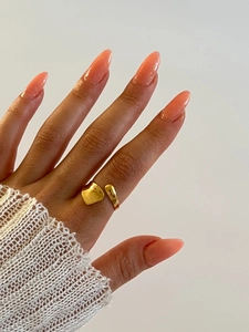 Gros plan d'une bague coeur dorée portée par un mannequin avec un poignet en tricot