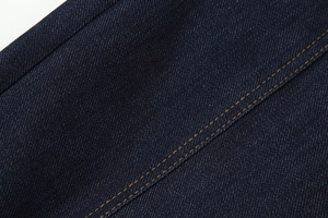 Détail macro de la texture du denim bleu foncé avec coutures contrastées orange sur jean
