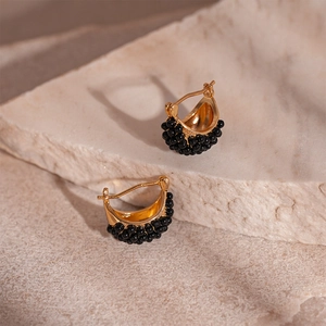 Close-up of vintage gold hoop earrings with black resin beads on a textured stone surface