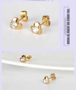 Detail of 18K gold heart studs with clear zircon stones on a white ceramic plate