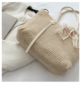 Detail view of straw tote bag featuring floral lace bow on a soft white fabric background