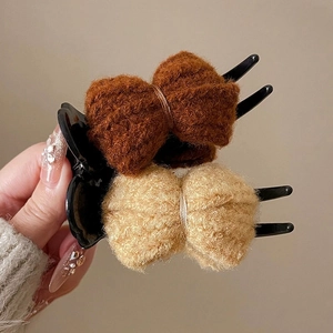 Detail of dark brown and beige plush bow hair clips held by a hand on beige background