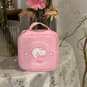 Pink square cosmetic bag with cute rabbit pattern and top handle on a floral table