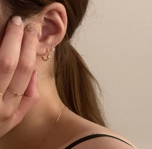 Detailed view of dainty gold earrings, necklace, and solitaire ring set on a model