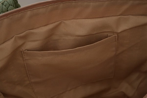 Detailed close-up of brown inner fabric pocket and zipper inside the woven tote bag