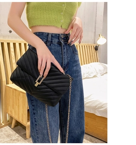 Detail of black quilted V-pattern handbag with gold chain strap and metal clasp closure