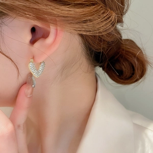 Close-up of asymmetrical gold heart earrings with white zircon on a model's ear
