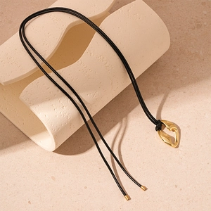 Detail of minimalist golden irregular geometric pendant on black cord sweater necklace