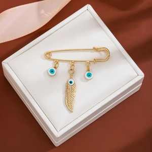 Macro shot of gold safety pin brooch with blue evil eye and feather charms in a jewelry box