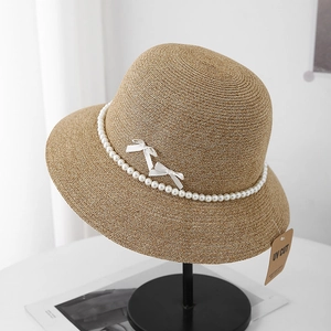 Detail of UV CUT straw sun hat with elegant pearl chain and white bows on display stand