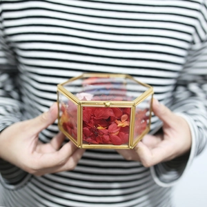 Modern hexagonal glass wedding ring box with gold metal frame and dried flower petals