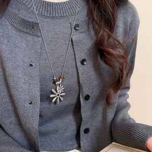 Close-up of long silver sweater chain featuring hollow daisy pendants and amber beads