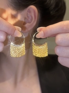 Detail of gold fringe C-shape hoop earring with luxurious mesh texture on model