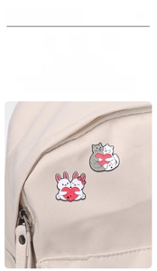 Detail of cute enamel pins with cats and rabbits holding red hearts on a canvas bag
