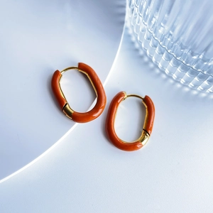 Macro shot of gold-plated U-shaped earrings featuring vibrant orange enamel inlay detail