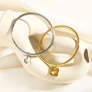 Detail of gold and silver stainless steel bangles with square pendants on ceramic