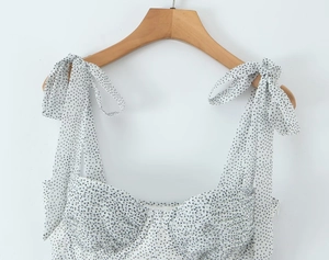 Close-up of white polka dot chiffon dress featuring adjustable tie shoulder straps and pleats